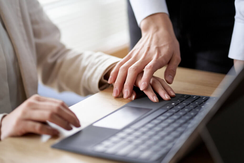 Picture of female worker at laptop with a male hand placed over hers