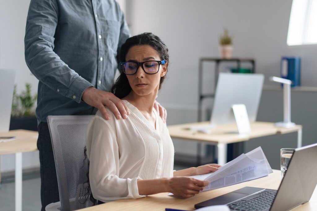 Beautiful young woman being victim of sexual harassment at workplace, copy space. Male boss touching his female secretary without permission at office. Corporate discrimination concept